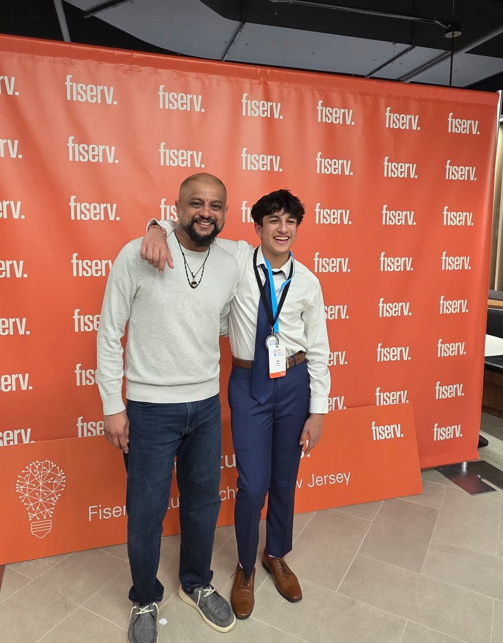 Vir Patel and his father at the Fiserv Future Techies finals in
                New Jersey, wearing a competitor badge and medal